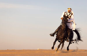 Saudi man riding an Arabian horse across the desert, showcasing Arabian horse riding techniques.